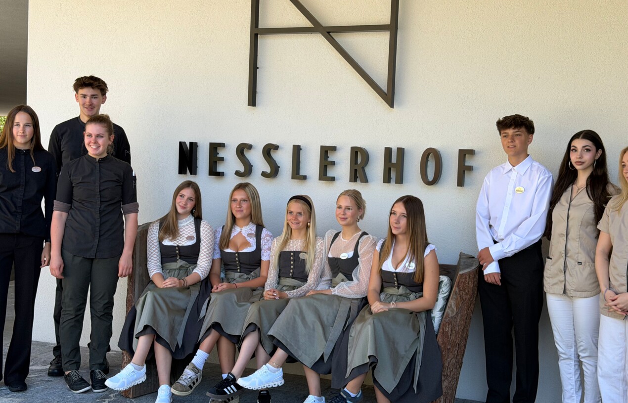 Junge Lerhlinge sitze auf einer Bank und dahinter das Nesslerhof Logo