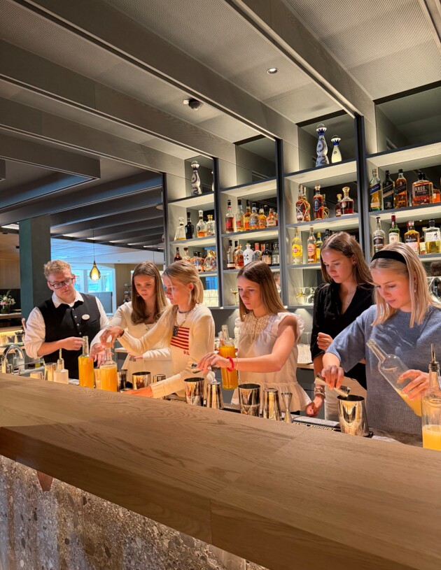 Junge Lerhlinge stehen hinter einer Bar und kreieren ihren Cocktail